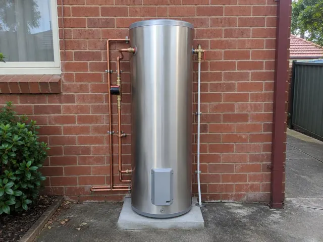 Stainless steel hot water cylinder on a concrete pad against a red brick wall in Arncliffe